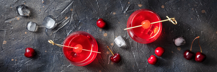 Cocktail garnished with cherry panorama, fresh cranberry juice with ice on a dark background, two...