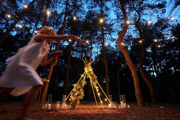 Festive string lights illumination on boho tipi arch decor on outdoor wedding ceremony venue in...