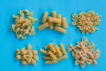 Fototapeta na wymiar Various kinds of uncooked pasta on the blue background, top view. Collection of different raw pasta on cooking table