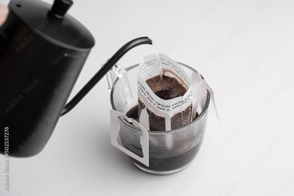 Wall mural black steel long spout drop kettle pouring hot water into a drip coffee bag in transparent cup. brew