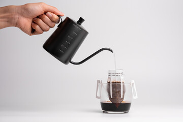 Handing holding black steel long spout drop kettle pouring hot water into a drip coffee bag in...