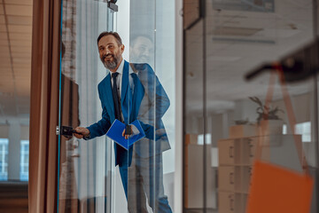 Smiling Caucasian man entering office space and holding notepad, copy space