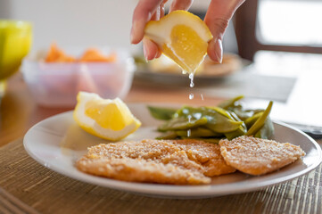 Hand queezing lemon on vegan chickpea cutlet.