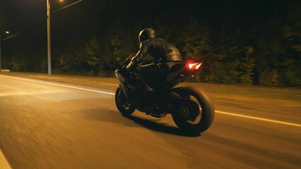 Young man in helmet riding fast on modern black sport motorbike at evening city street. Motorcyclist racing his motorcycle on night empty road. Guy driving bike. Concept of freedom and hobby. Close up