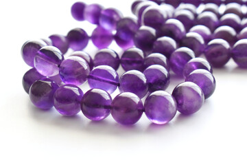 Amethyst gemstone bead strand on the table.  Purple or violet crystal stone on white background. 