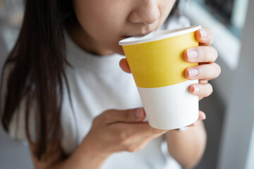 Close up of the Asian lady holding the hot drink paper cup with one hand and sipping the hot beverage