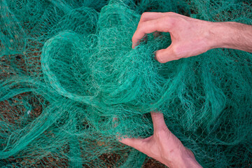 View of a man hands picking up a green fishing net. Waste in nature. Environmental Protection.