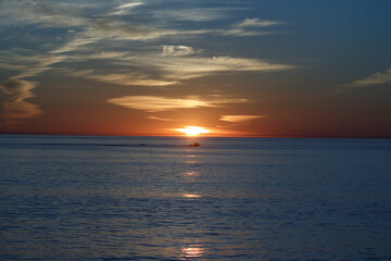 Naklejka premium sunset over the ocean with boat in the distance.