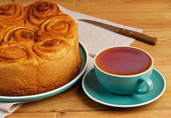 Closeup homemade cinnamon rolls from yeast dough and cup of tea on wooden table.