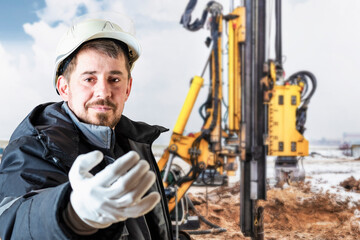 A male builder in a white hard hat against a blurred background of a construction site with a blue sky. Positive civil engineer with a beard.