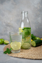 Detox Sassy water with lemon, cucumber, mint. A bottle of clean, cool and fresh drink stands on a gray concrete background with ingredients on board. Strengthening immunity, diet.