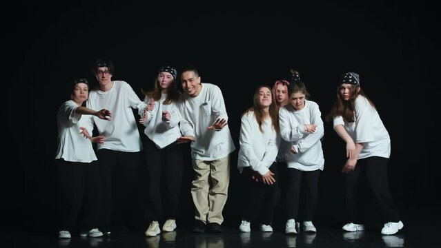 A group of young dancers in white T-shirts on a black background perform free dance movements, they finish the dance with a synchronized final pose