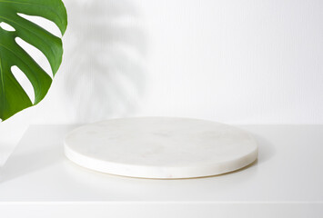White marble podium for product presentation with tropical tree leaves