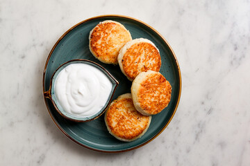 Fried, Cottage cheese pancakes, with sour cream, Cheesecakes, on a marble table, top view, no people.
