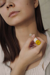 Crop serene woman applying roller perfume or essential oil on neck and enjoying aromatic scent...