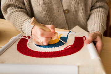 Close up of woman creating a handmade decoration for home. Female pushing the punchneedle straight down into the fabric. Hobby, DIY, handycraft concept. New trend in embroidery Punch needle.