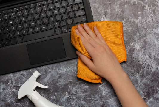Cleaning a laptop keyboard with a rag and cleansing spray bottle