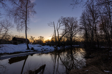 Winter landscape, trees near the river against the backdrop of sunset.