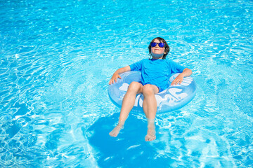 Boy wearing sun glasses, relaxing on an inflatable swim ring in a sunny day, spending time in a...