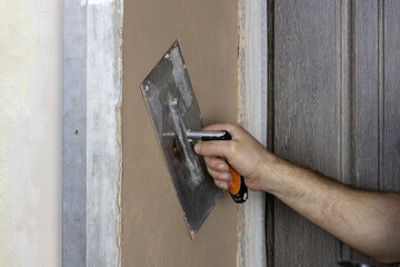 A worker applies plaster to a wall with a spatula.