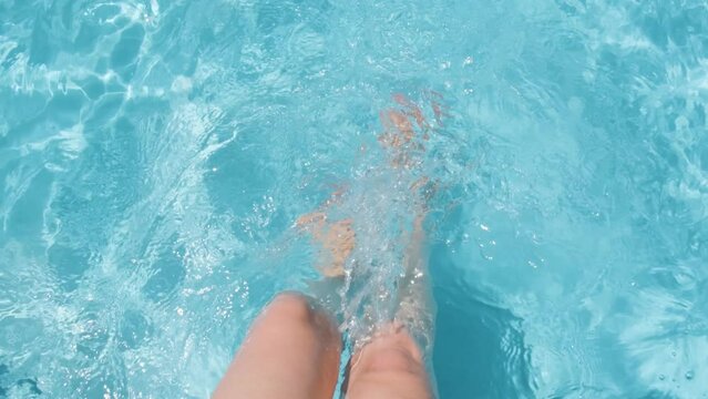 Female sitting on poolside, splashing water with legs, Clear crystal water in Slow motion