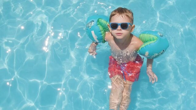Cute Caucasian boy Relaxing on Swimming pool wearing sunglasses and floaters, Summer concept. Topshot