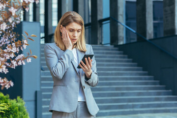 Frustrated and shocked business woman reading bad news online from phone, businesswoman outside office in business suit