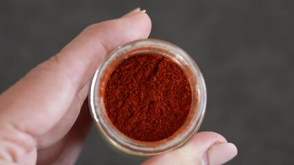 Closeup view 4k stock video footage of grounded into powder red smoked paprika pepper isolated in glass container. Woman holding glass bottle full of fry grounded powder red pepper spices