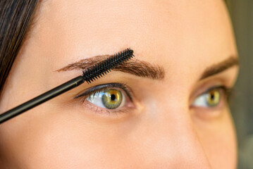 woman with permanent eyebrow makeup and eyebrow brush looks away, self-care, beautiful well groomed eyebrows, trendy microblading technique