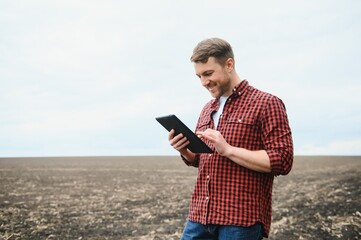 A farmer in boots works with his tablet in a field sown in spring. An agronomist walks the earth,...