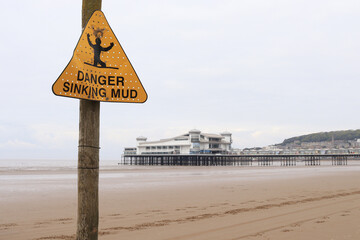 'DANGER SINKING MUD' sign with Weston-super-Mare's Grand Pier in the background - obrazy, fototapety, plakaty