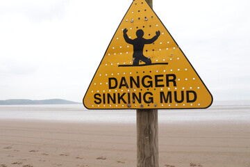 'DANGER SINKING MUD' sign with background of seemingly endless mud where the sea should be - obrazy, fototapety, plakaty