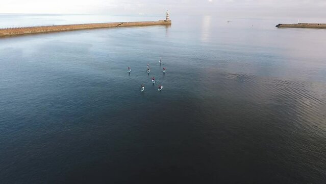A group of people paddle boarding on a still sea at Roker Beach Sunderland, aerial drone shot.