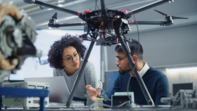 Skilful Male Engineer with Semiconductor Give Advices to Black Female Computer Developer While she Write Code for Drone Programme. Startup Concept. Portrait View