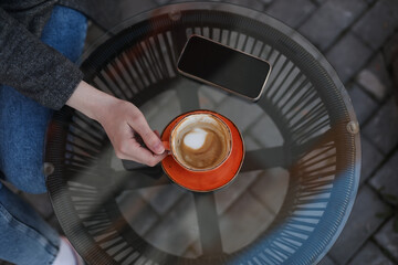 Woman's hands holding a big orange coffee cup.