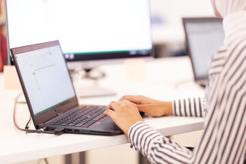 African american muslim girl with hijab working on a laptop in modern office..