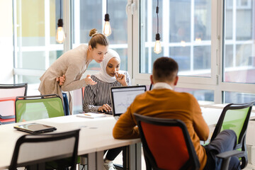 Creative team of young individuals working on desktop and laptop computers in a modern office space..