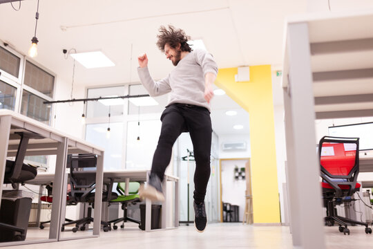 Young businessman with clumsy hair having fun at the office. Man jumping and dancing celebrating success.