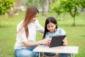 A mother is teaching her daughter online on a digital tablet or watching a video clip on a tablet together.