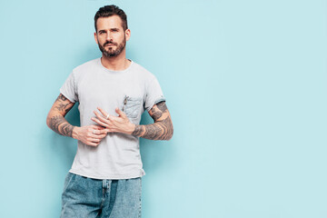 Portrait of handsome confident stylish hipster lambersexual model. Sexy man dressed in T-shirt and jeans. Fashion male isolated on blue wall in studio