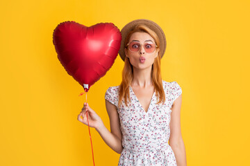 positive young woman in straw hat and sunglasses hold love heart balloon on yellow background
