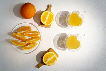 Fresh orange juice in glass with leaves, sliced oranges and ice on white background. Top view