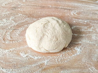 Fresh raw dough on wooden table covered with flour. Top view