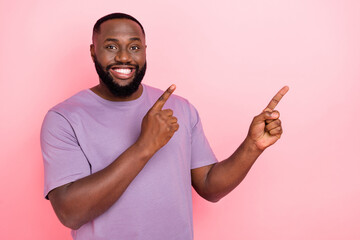 Photo of pretty funny guy wear purple t-shirt pointing two fingers empty space isolated pink color background