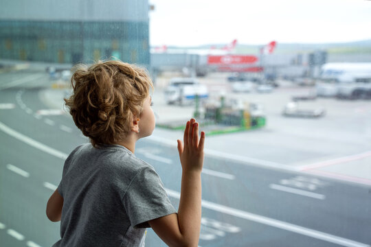 Child looking out window at airplane in airport, while waiting for boarding in transit hall near departure gate. Family travel by air with child.