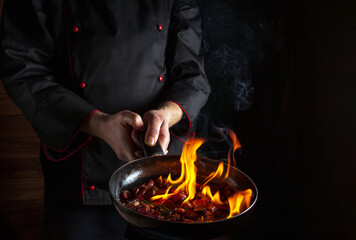 Professional chef prepares vegetable food in a frying pan with a flame of fire. The concept of...