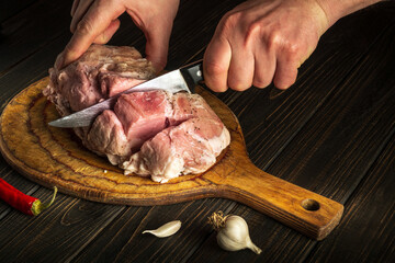 Professional chef cuts meat with a knife before baking. Spices on the kitchen table in a restaurant for preparing a delicious lunch or dinner.