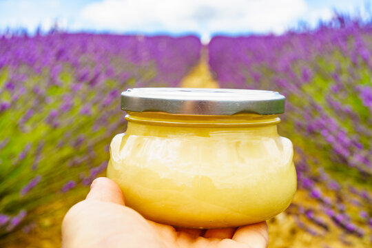 Hand holds jar with honey against lavender flowers.