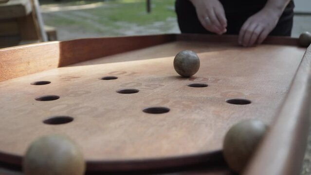 Caucasian hands of unrecognizable woman roll wooden balls up inclined board of Japanese billiards to get into the hole. One ball hits the target with game points 80, close-up.