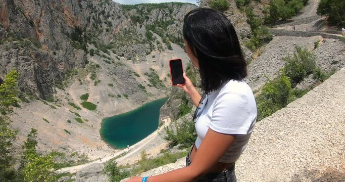 Side view of young female tourist enjoy walking makes shooting on mobile phone during travel on Blue Lake Modro Jezero in Croatia
